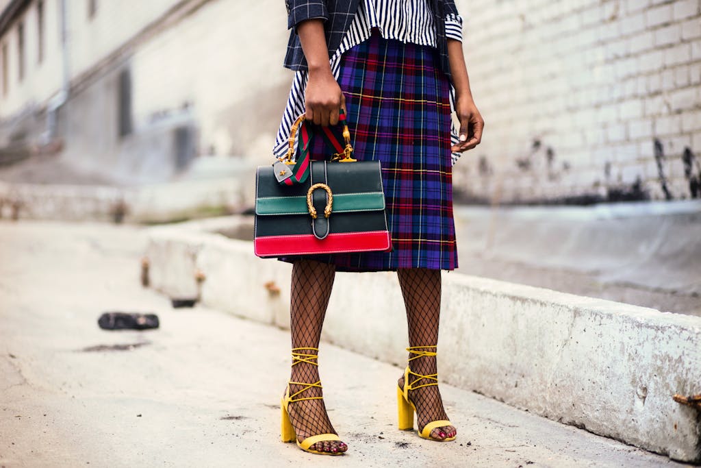 Fashion-forward outfit with plaid skirt and colorful handbag in urban setting.