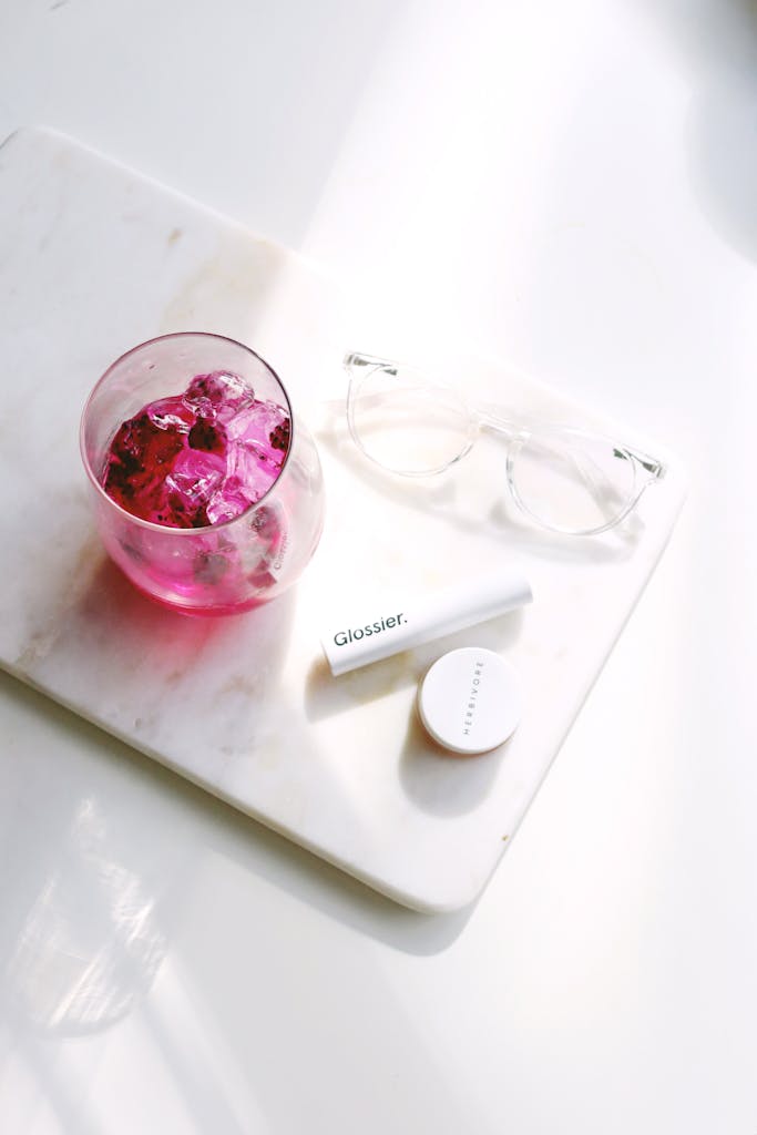 Flat lay of cosmetics with pink drink on marble, perfect for beauty and lifestyle themes.